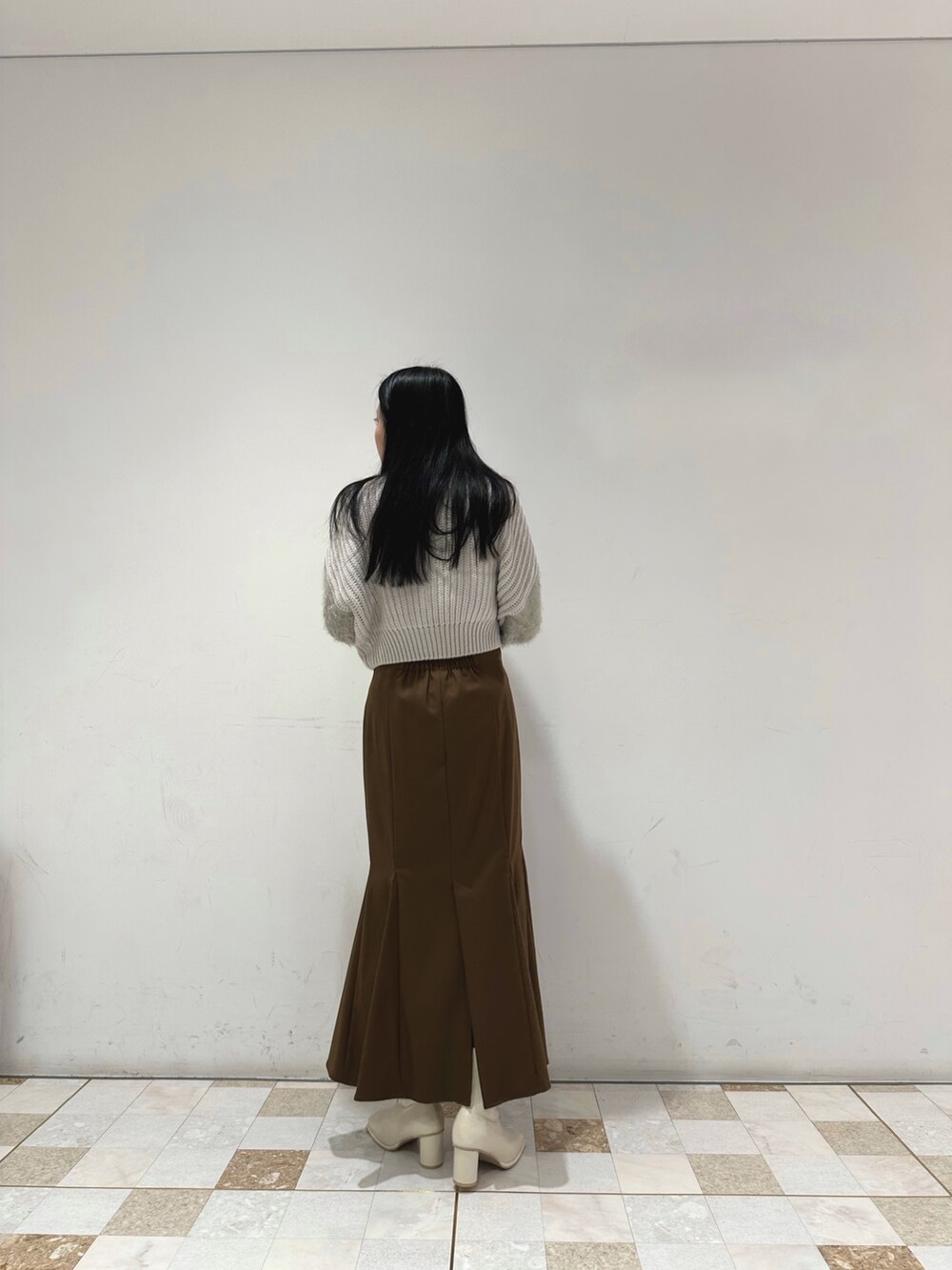 ブラウン系のスカート、グレー系のニット/セーター、ホワイト系のブーツを着用したレディースの冬コーディネートの3枚目の写真