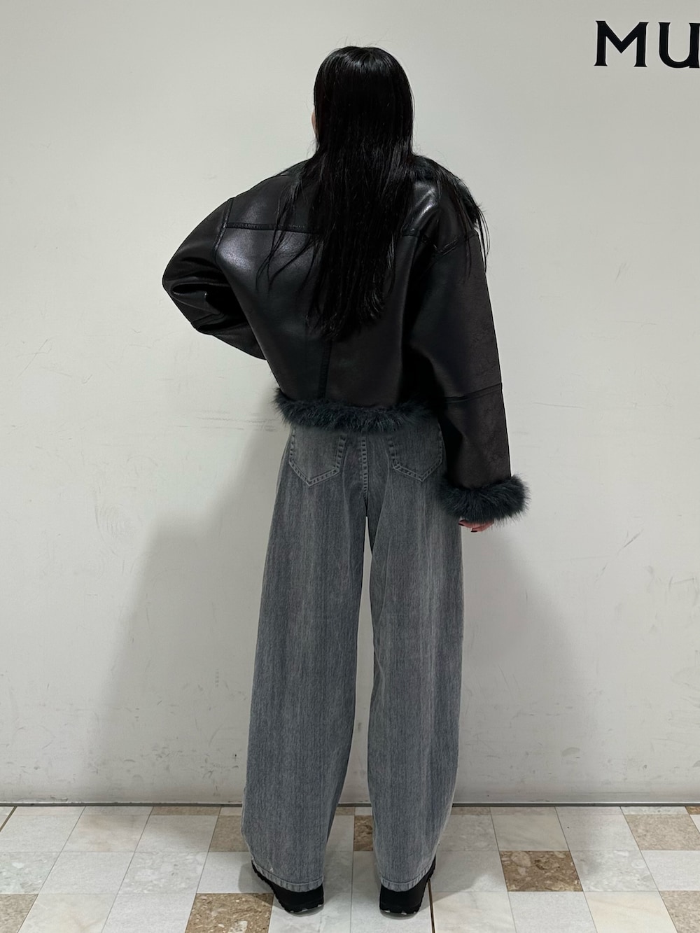 グレー系のデニムパンツ、ブラック系のブーツ、ブラック系のムートンコートを着用したレディースの夏コーディネートの2枚目の写真