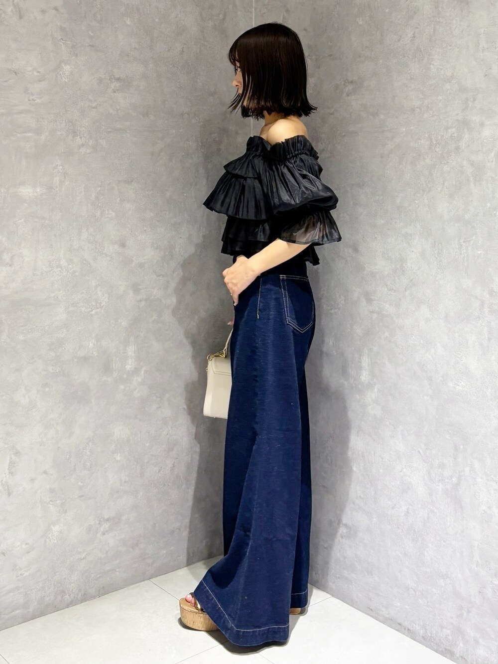 ブルー系のデニムパンツ、ブラウン系のサンダル、ホワイト系のハンドバッグを着用したレディースの夏コーディネートの4枚目の写真