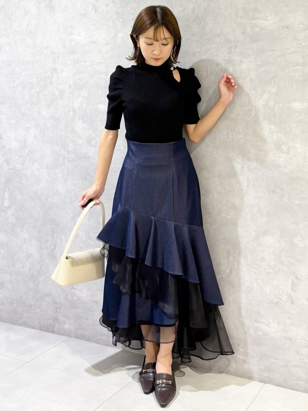 ブルー系のスカート、ブラック系のニット/セーター、ブラウン系のパンプスを着用したレディースの春コーディネートの6枚目の写真