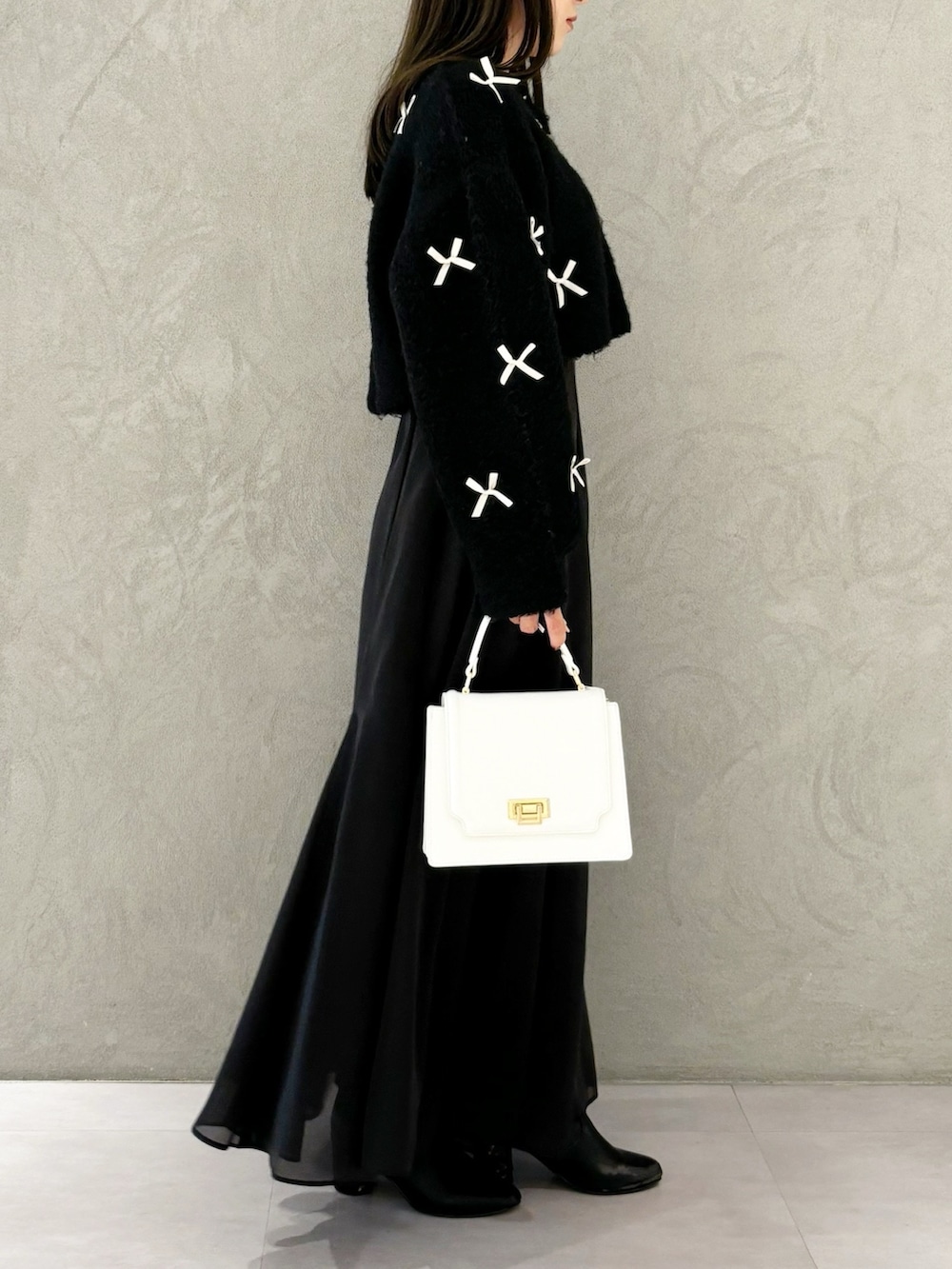 ブラック系のスカート、ブラック系のブーツ、ホワイト系のハンドバッグを着用したレディースの冬コーディネートの6枚目の写真