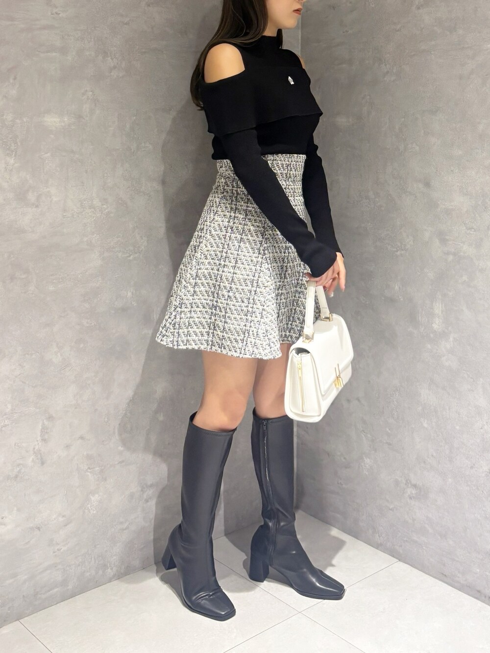 ブラック系のブーツ、ホワイト系のハンドバッグ、ブラック系のニット/セーターを着用したレディースの冬コーディネートの2枚目の写真