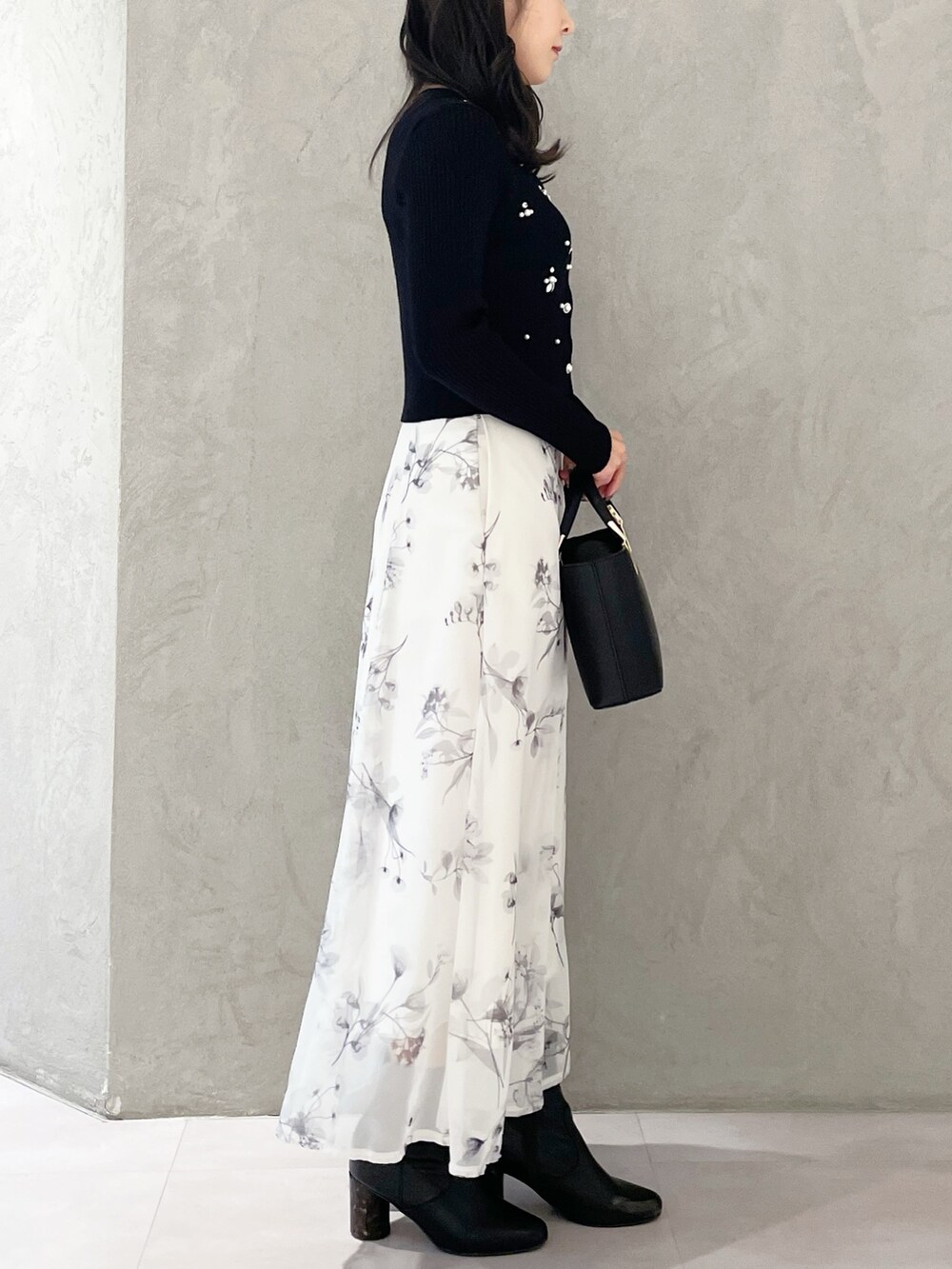 ブラック系のハンドバッグ、ブラック系のブーツ、ホワイト系のスカートを着用したレディースの冬コーディネートの3枚目の写真