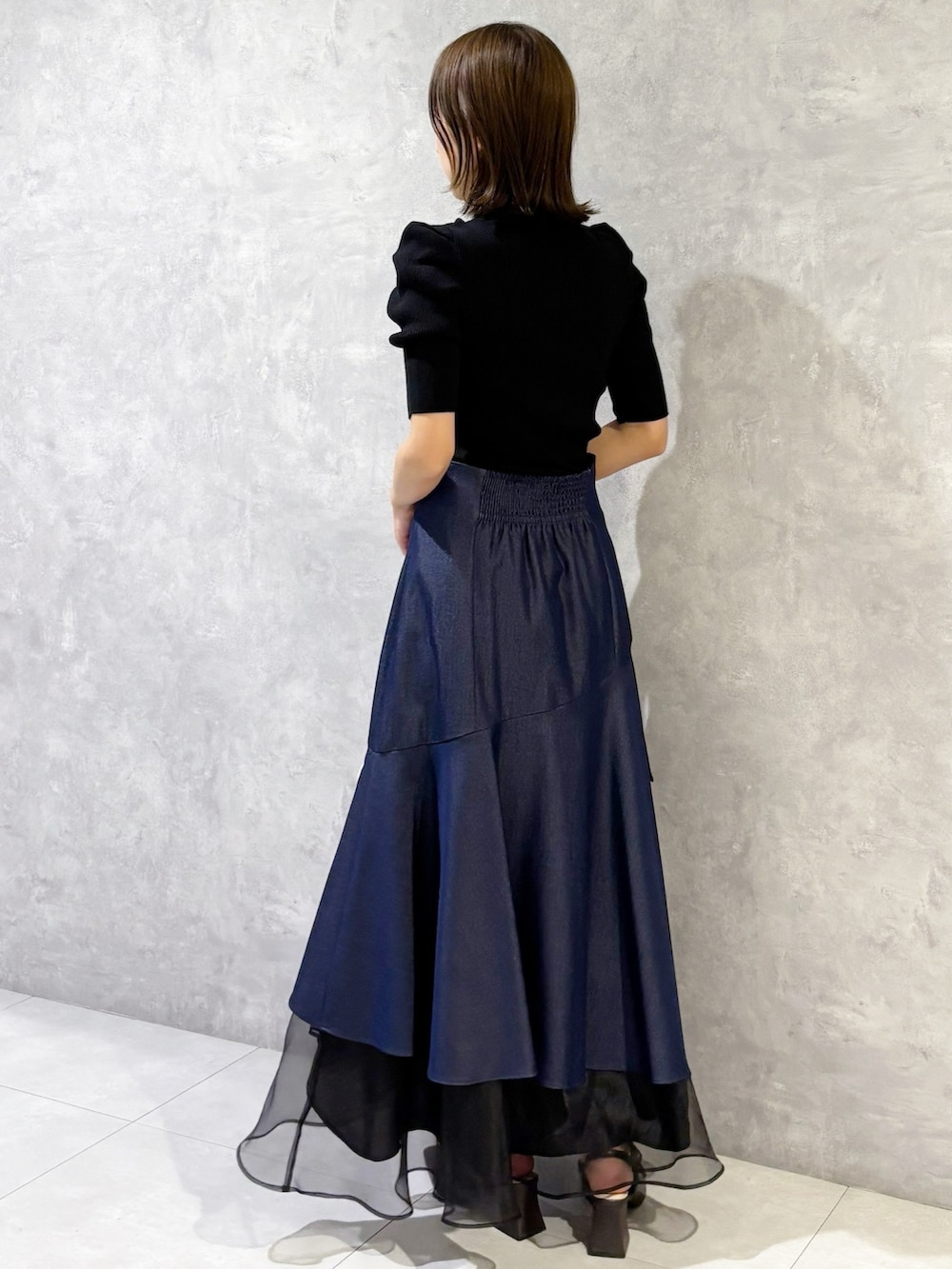 ブルー系のスカート、ブラック系のニット/セーター、ブラウン系のパンプスを着用したレディースの春コーディネートの5枚目の写真