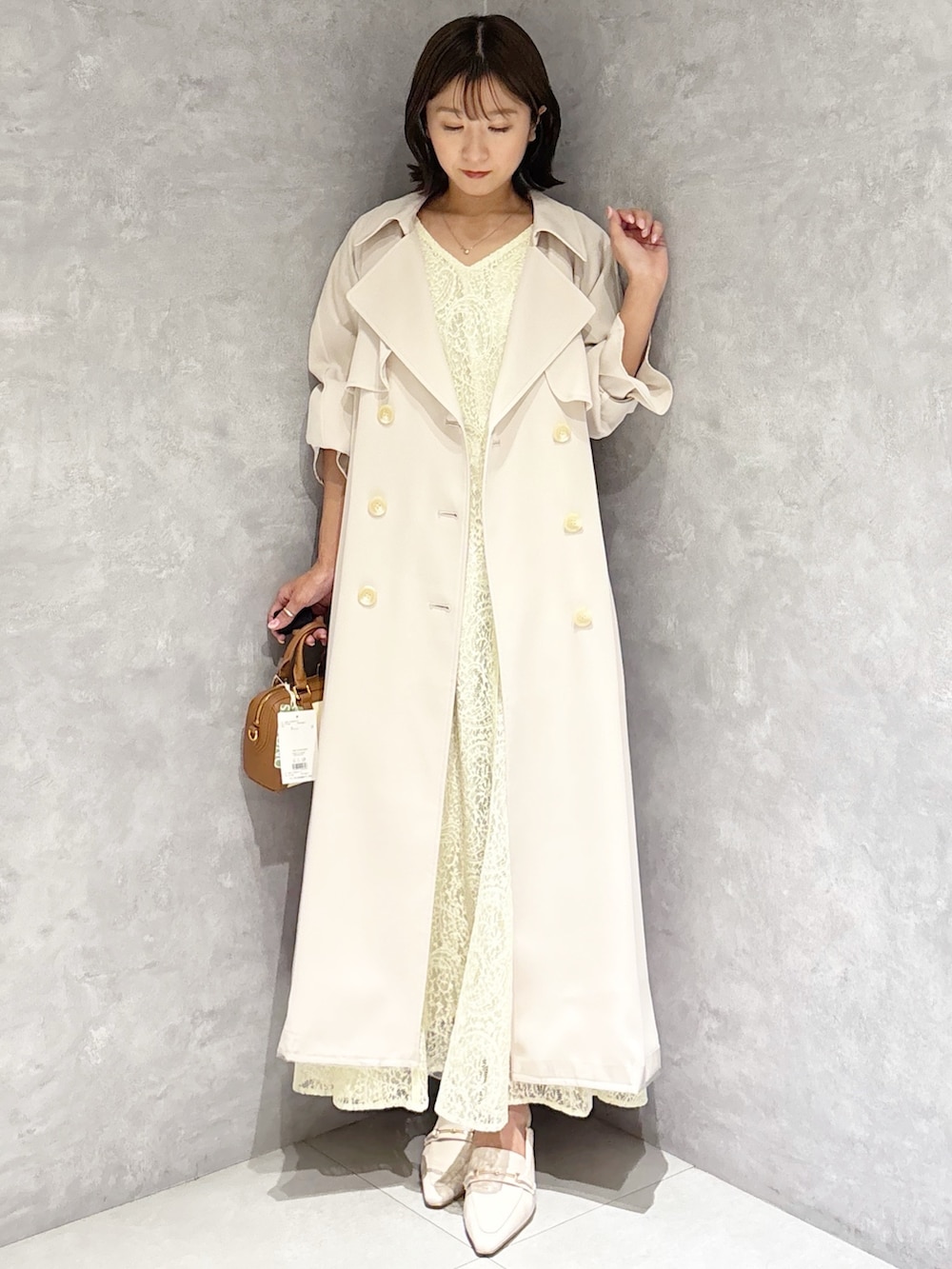 イエロー系のワンピース、ホワイト系のパンプス、ブラウン系のハンドバッグを着用したレディースの春コーディネートの5枚目の写真