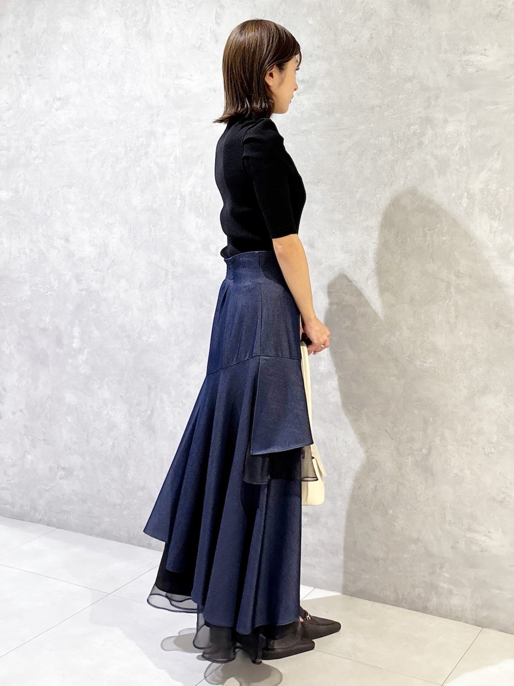 ブルー系のスカート、ブラック系のニット/セーター、ブラウン系のパンプスを着用したレディースの春コーディネートの3枚目の写真