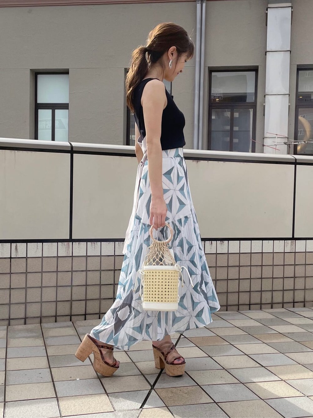 ブルー系のスカート、ホワイト系のハンドバッグ、ブラック系のニット/セーターを着用したレディースの夏コーディネートの3枚目の写真