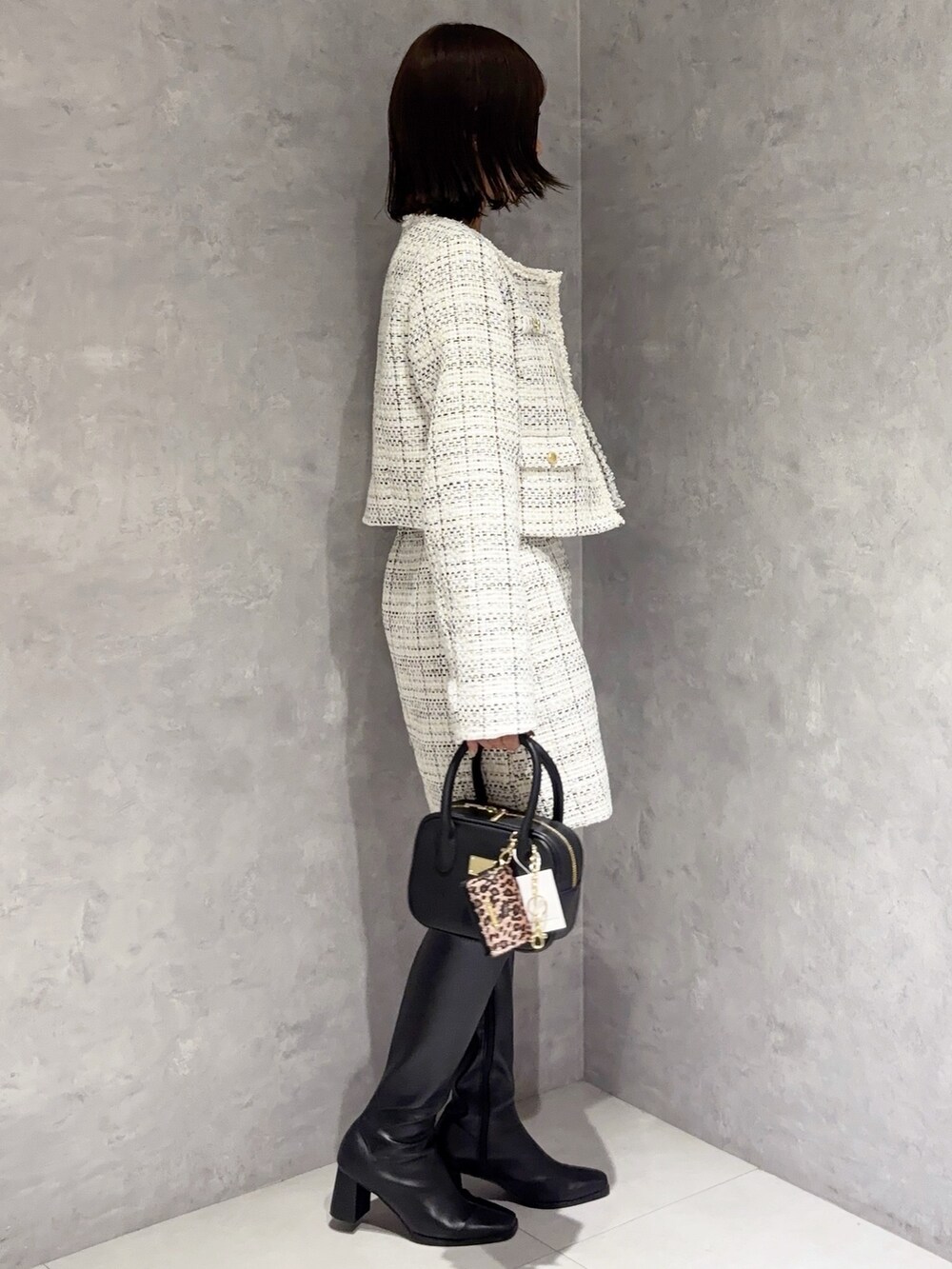 ホワイト系のスカート、ブラック系のブーツ、ブラック系のハンドバッグを着用したレディースの秋コーディネートの2枚目の写真