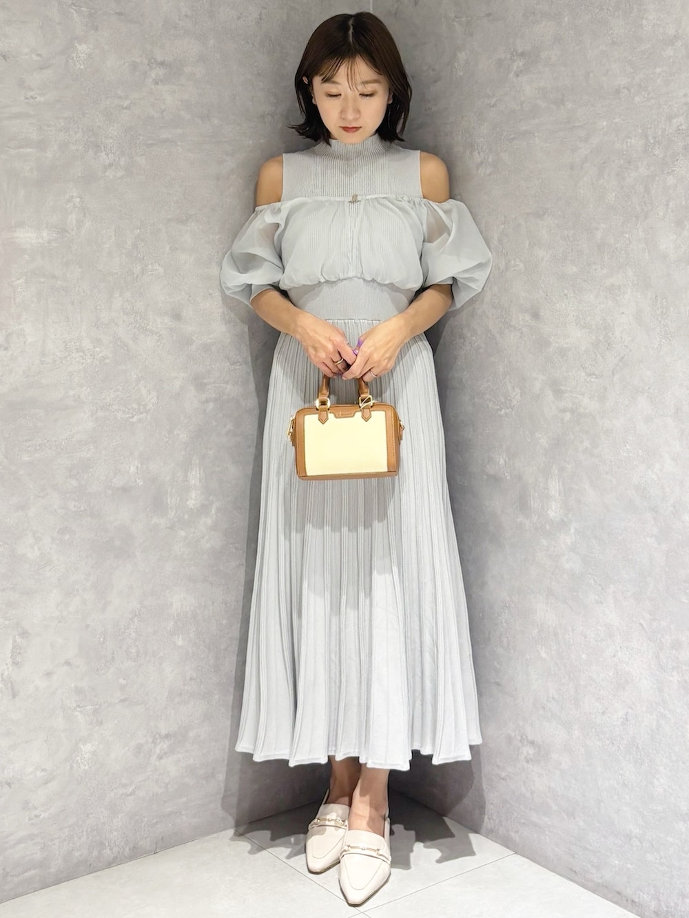 グレー系のワンピース、ホワイト系のパンプス、ブラウン系のハンドバッグを着用したレディースの春コーディネートの6枚目の写真