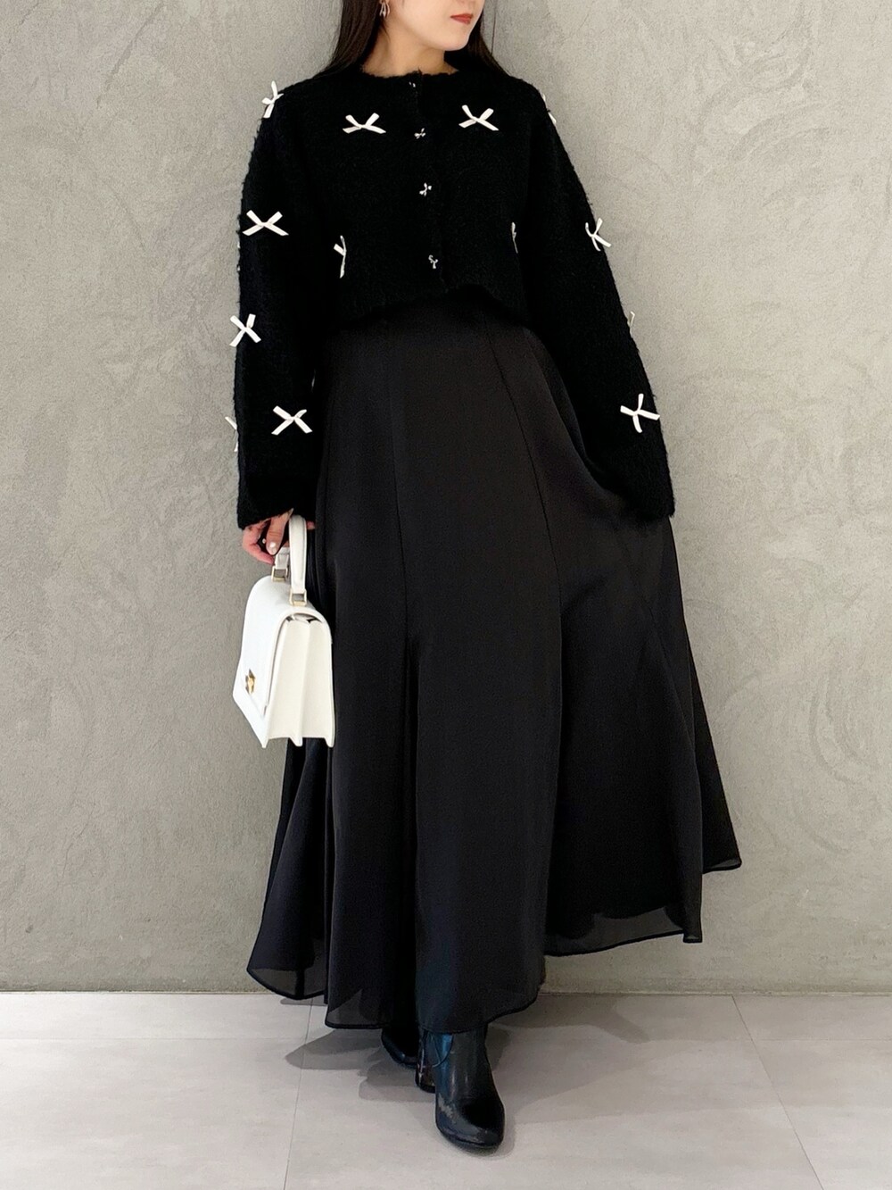 ブラック系のスカート、ブラック系のブーツ、ホワイト系のハンドバッグを着用したレディースの冬コーディネートの7枚目の写真