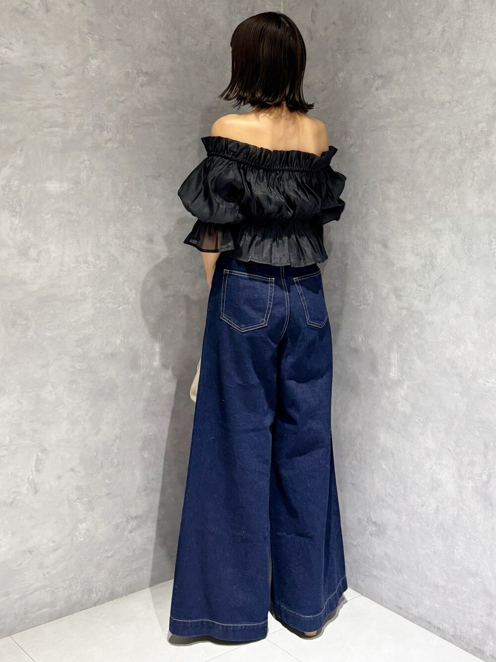 ブルー系のデニムパンツ、ブラウン系のサンダル、ホワイト系のハンドバッグを着用したレディースの夏コーディネートの2枚目の写真