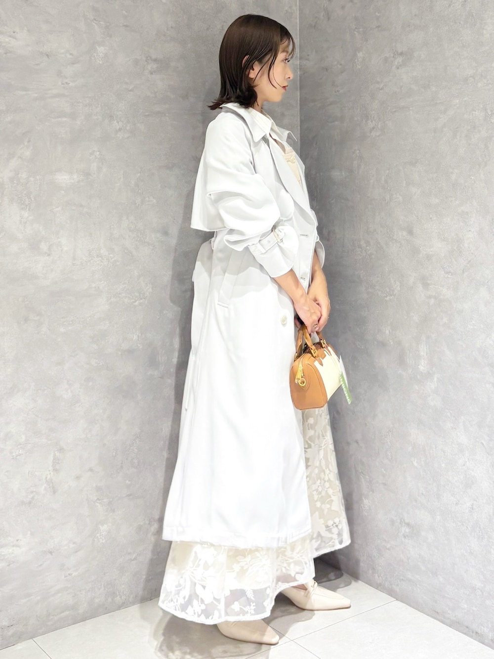 ブルー系のトレンチコート、ベージュ系のワンピース、ブラウン系のハンドバッグを着用したレディースの春コーディネートの2枚目の写真