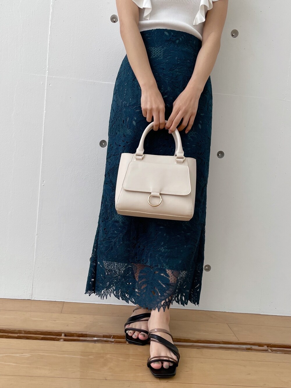 グリーン系のスカート、ブラック系のサンダル、ホワイト系のハンドバッグを着用したレディースの春コーディネートの2枚目の写真