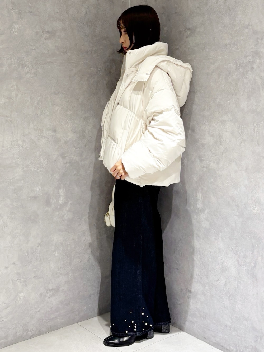 ブルー系のデニムパンツ、ホワイト系のダウンジャケット/コート、ベージュ系のニット/セーターを着用したレディースの秋コーディネートの2枚目の写真