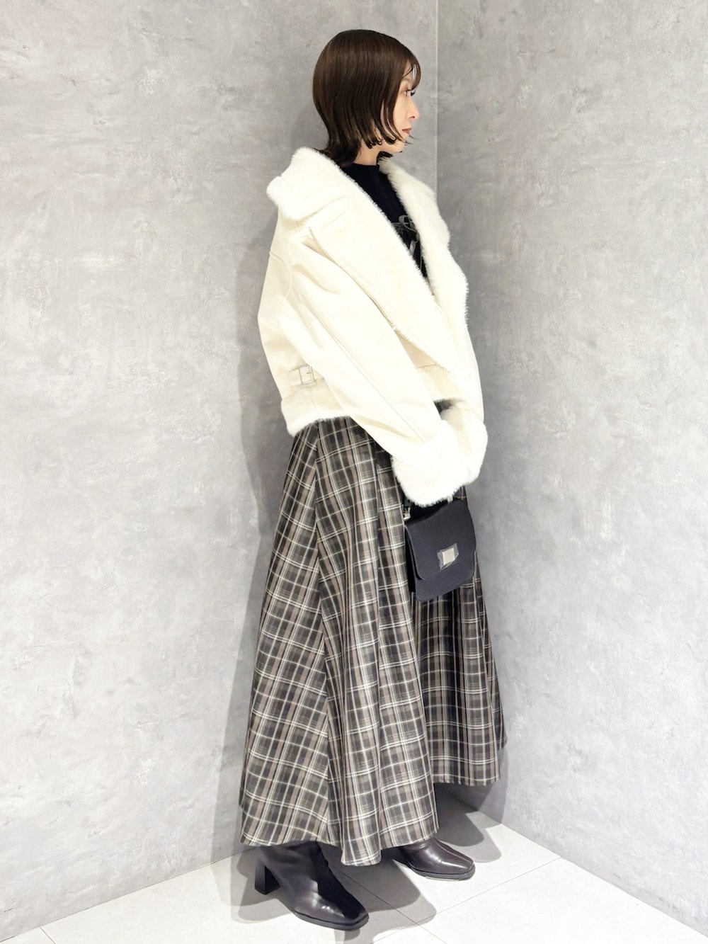 ブラック系のニット/セーター、ホワイト系のムートンコート、ブラック系のハンドバッグを着用したレディースの冬コーディネートの2枚目の写真