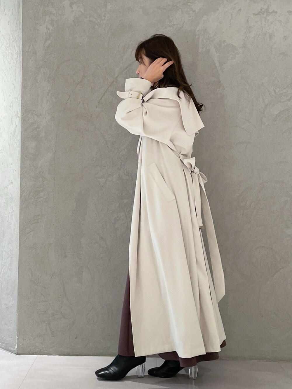 パープル系のワンピース、ブラック系のブーツ、ホワイト系のトレンチコートを着用したレディースの冬コーディネートの2枚目の写真