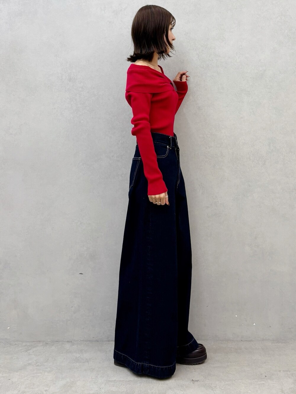 レッド系のニット/セーター、ブルー系のデニムパンツ、ブラウン系のブーツを着用したレディースの秋コーディネートの2枚目の写真