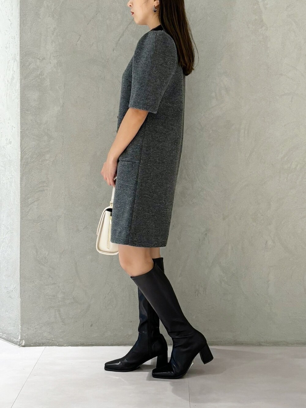 ブラック系のブーツ、ホワイト系のショルダーバッグ、グレー系のワンピースを着用したレディースの秋コーディネートの2枚目の写真