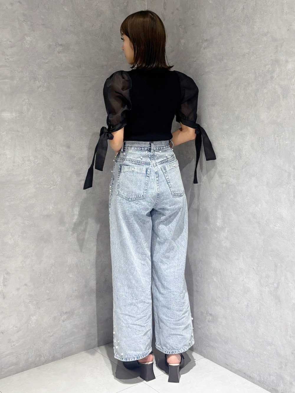 ブルー系のデニムパンツ、ブラック系のニット/セーター、ホワイト系のハンドバッグを着用したレディースの春コーディネートの3枚目の写真