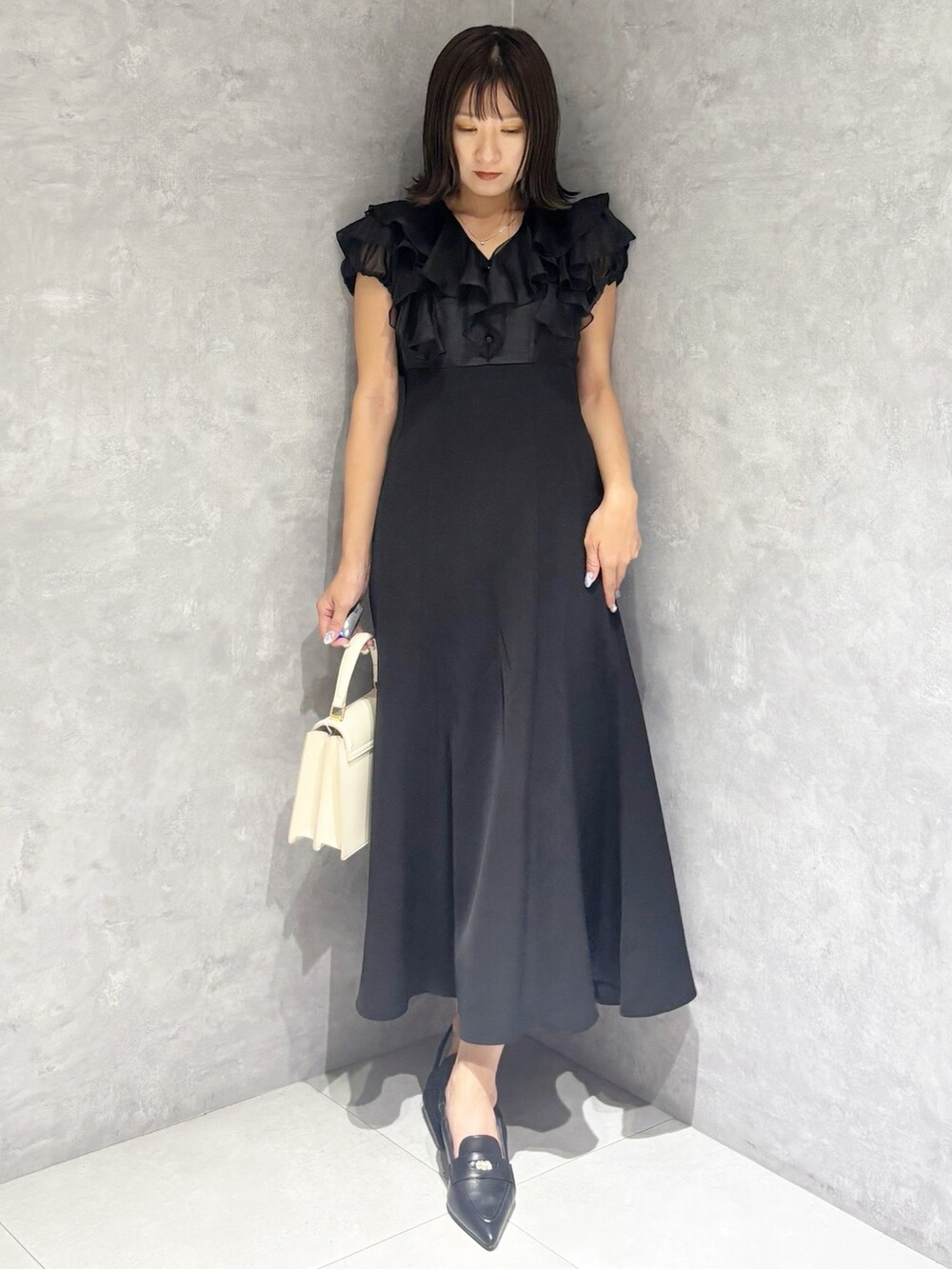 ブラック系のワンピース、ブラック系のパンプス、ホワイト系のハンドバッグを着用したレディースの夏コーディネートの5枚目の写真