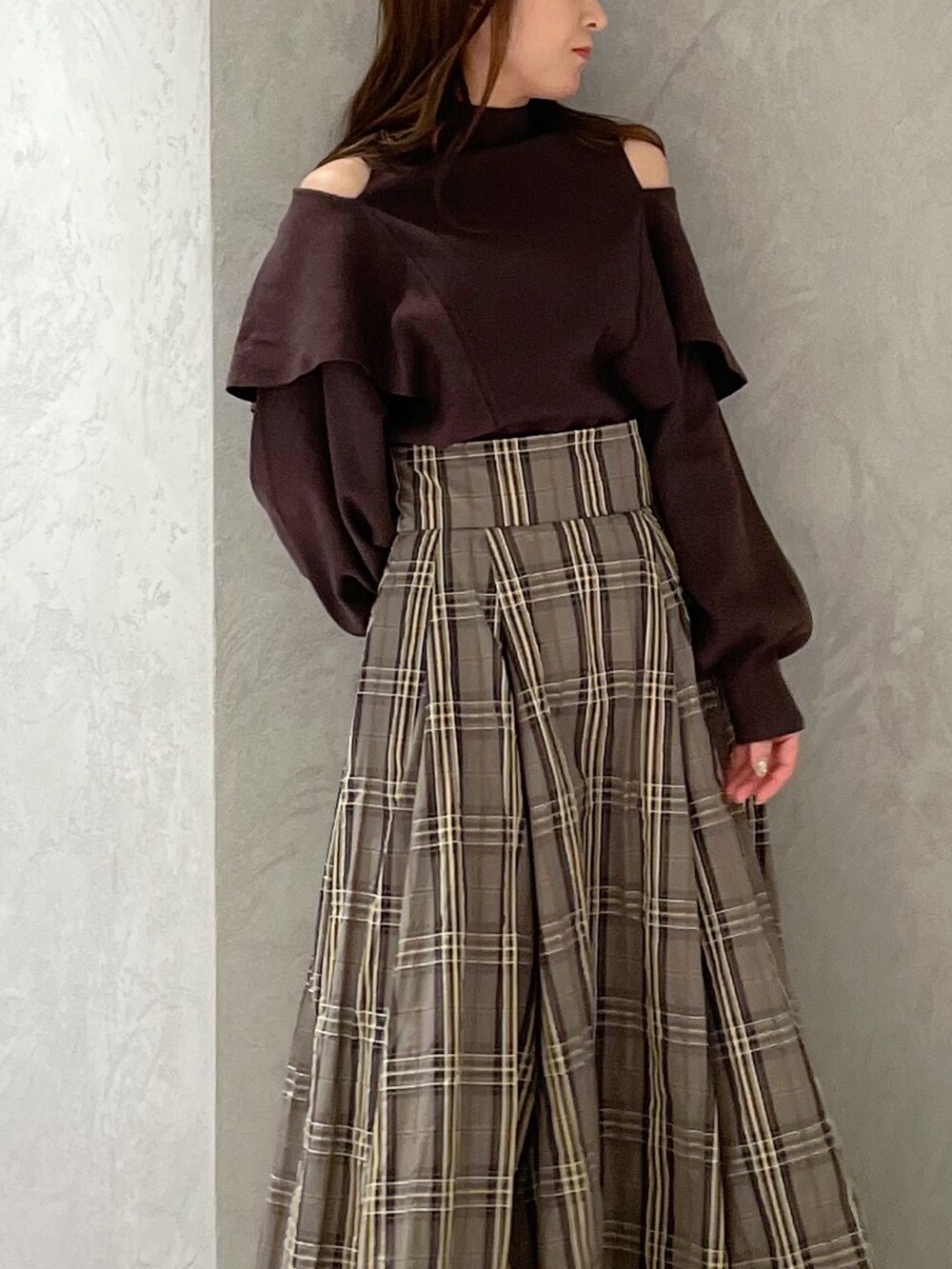 ベージュ系のスカート、ブラウン系のニット/セーター、ブラック系のブーツを着用したレディースの秋コーディネートの2枚目の写真