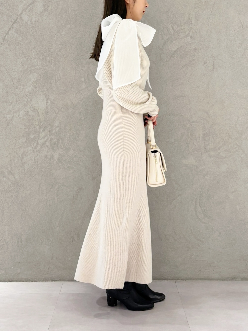 ホワイト系のハンドバッグ、ブラック系のブーツ、ホワイト系のワンピースを着用したレディースの冬コーディネートの6枚目の写真