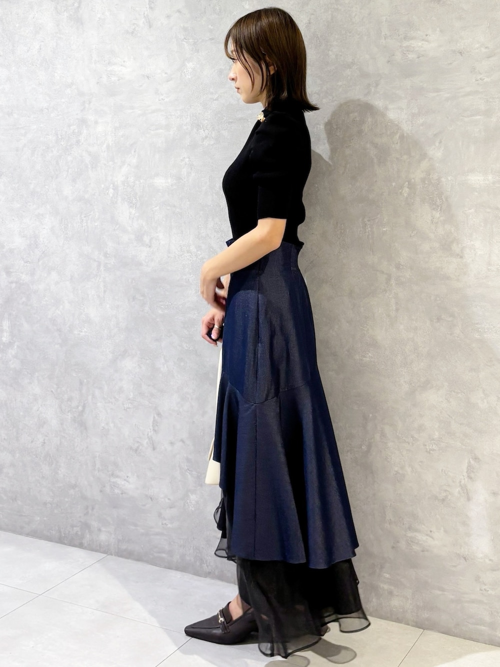 ブルー系のスカート、ブラック系のニット/セーター、ブラウン系のパンプスを着用したレディースの春コーディネートの2枚目の写真