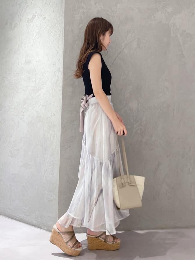 ピンク系のスカート、ブラック系のニット/セーター、ベージュ系のトートバッグを着用したレディースの夏コーディネートの3枚目の写真