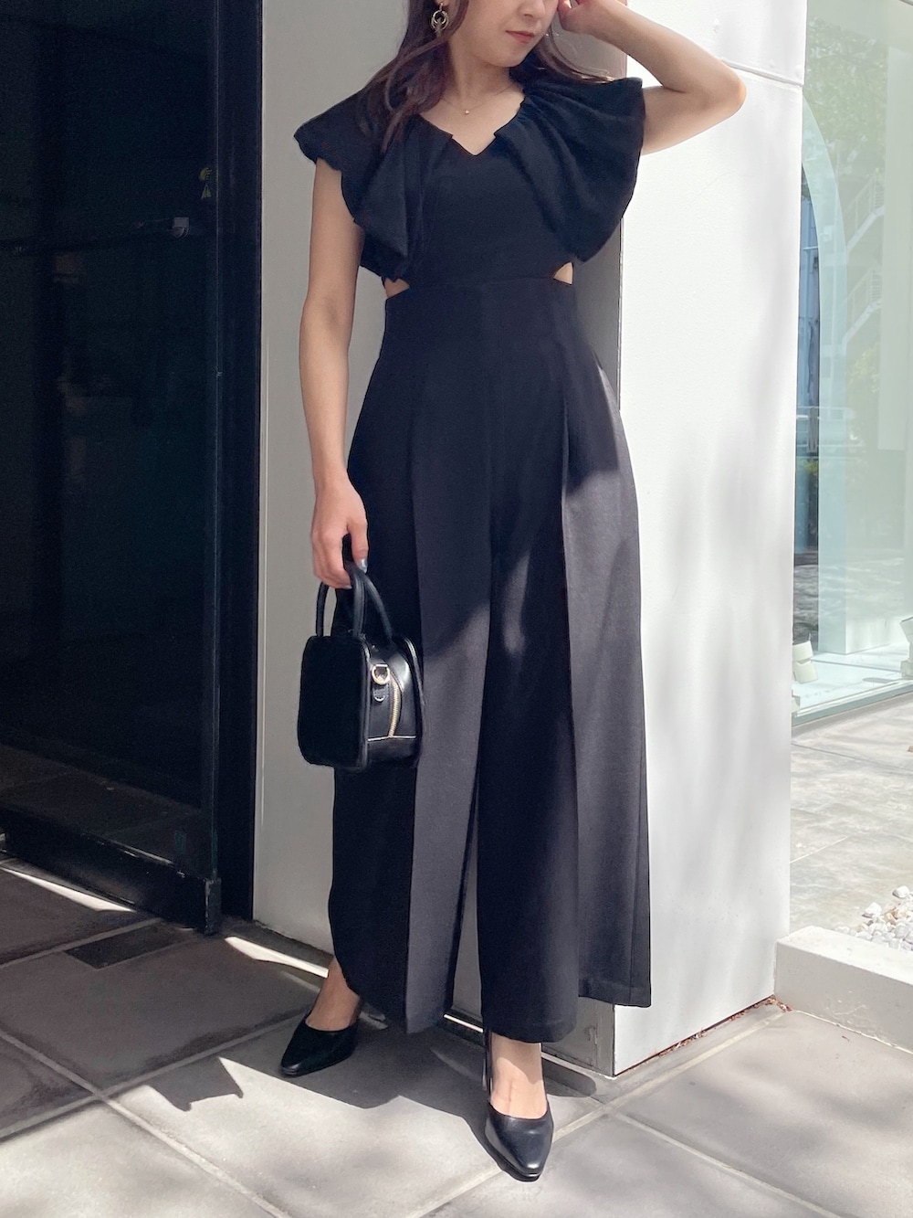 ブラック系のハンドバッグ、ブラック系のパンプス、ブラック系のつなぎ/オールインワンを着用したレディースの春コーディネートの3枚目の写真