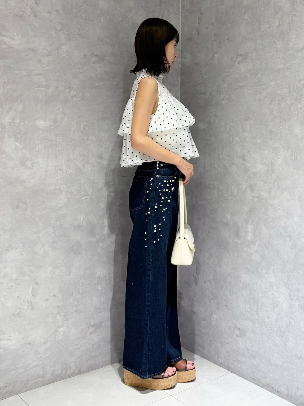 ブルー系のデニムパンツ、ブラウン系のサンダル、ホワイト系のハンドバッグを着用したレディースの夏コーディネートの3枚目の写真