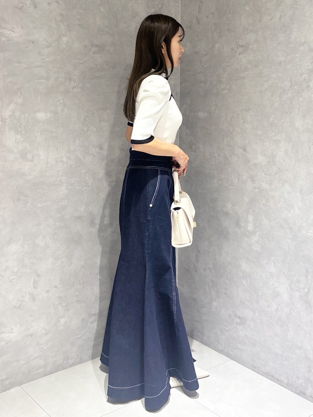 ブルー系のスカート、ホワイト系のパンプス、ホワイト系のハンドバッグを着用したレディースの春コーディネートの5枚目の写真