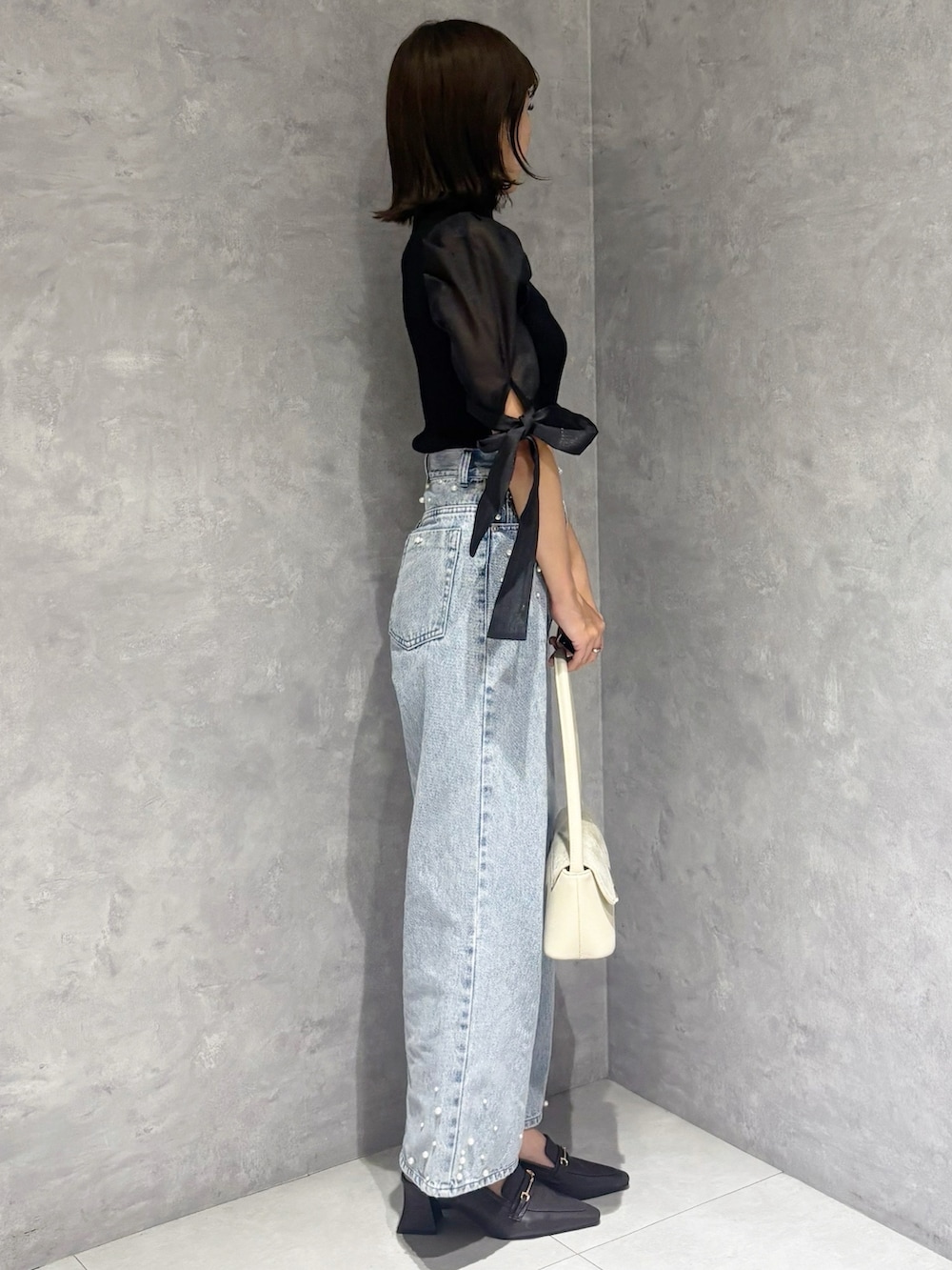 ブルー系のデニムパンツ、ブラック系のニット/セーター、ホワイト系のハンドバッグを着用したレディースの春コーディネートの5枚目の写真