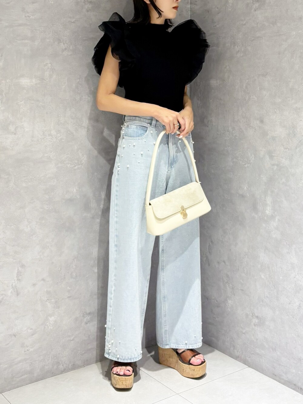 ブルー系のデニムパンツ、ブラック系のニット/セーター、ホワイト系のハンドバッグを着用したレディースの春コーディネートの2枚目の写真