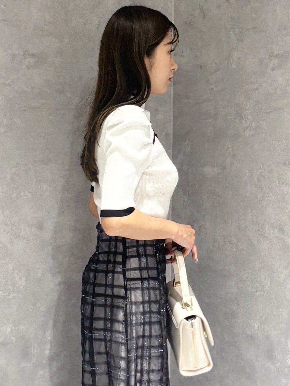ブルー系のスカート、ブラック系のパンプス、ホワイト系のハンドバッグを着用したレディースの春コーディネートの2枚目の写真