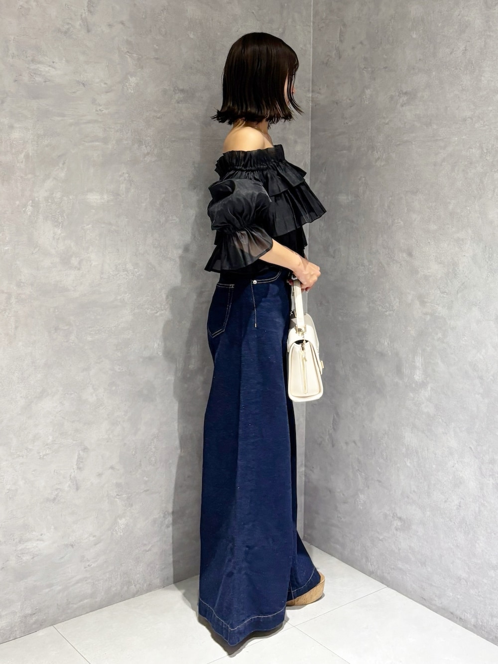 ブルー系のデニムパンツ、ブラウン系のサンダル、ホワイト系のハンドバッグを着用したレディースの夏コーディネートの3枚目の写真