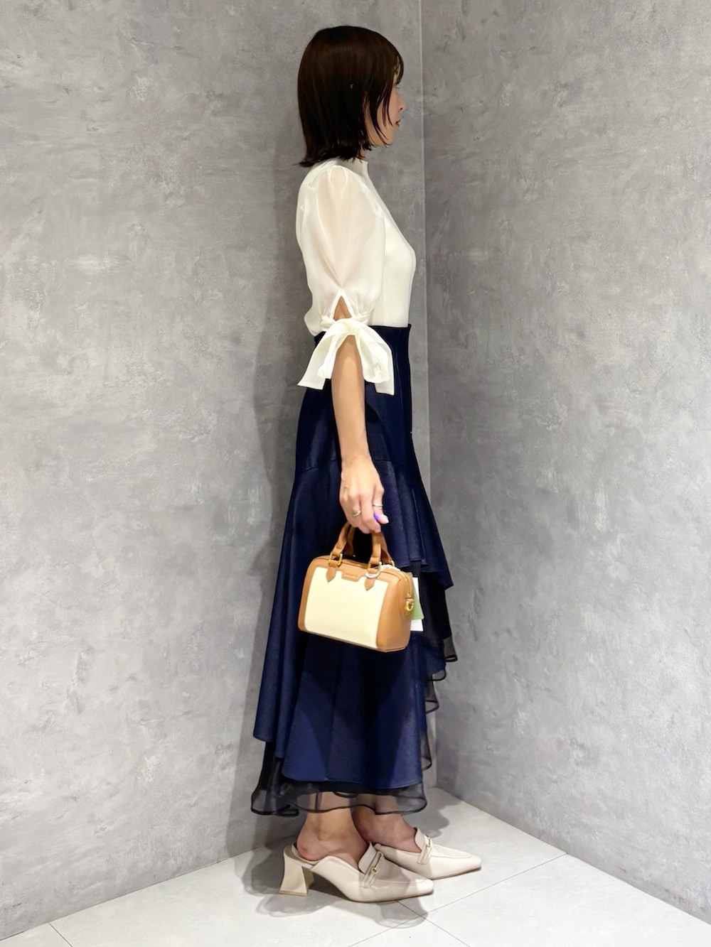 ブルー系のスカート、ホワイト系のニット/セーター、ホワイト系のパンプスを着用したレディースの春コーディネートの4枚目の写真