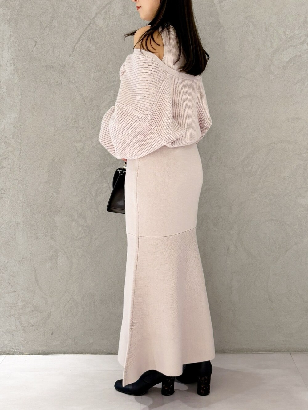 ブラウン系のハンドバッグ、ピンク系のワンピース、ブラック系のブーツを着用したレディースの冬コーディネートの2枚目の写真