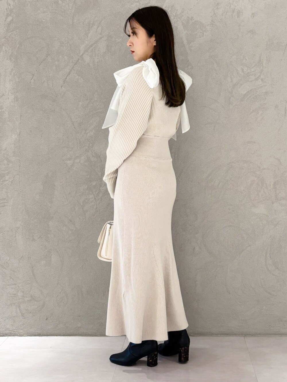 ホワイト系のハンドバッグ、ブラック系のブーツ、ホワイト系のワンピースを着用したレディースの冬コーディネートの2枚目の写真