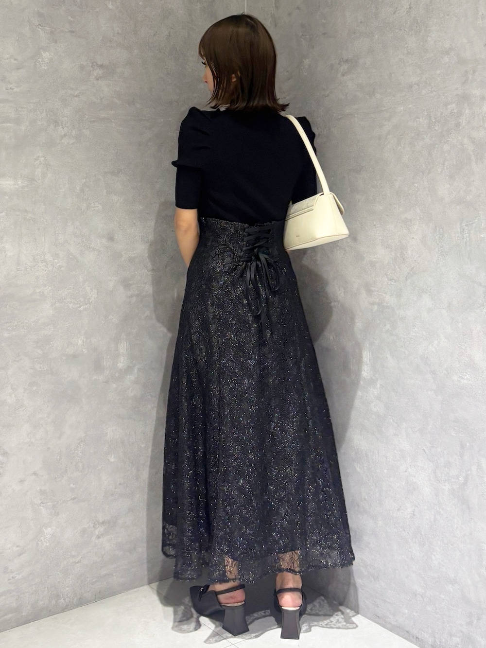 ブラック系のスカート、ブラック系のニット/セーター、ホワイト系のハンドバッグを着用したレディースの春コーディネートの3枚目の写真