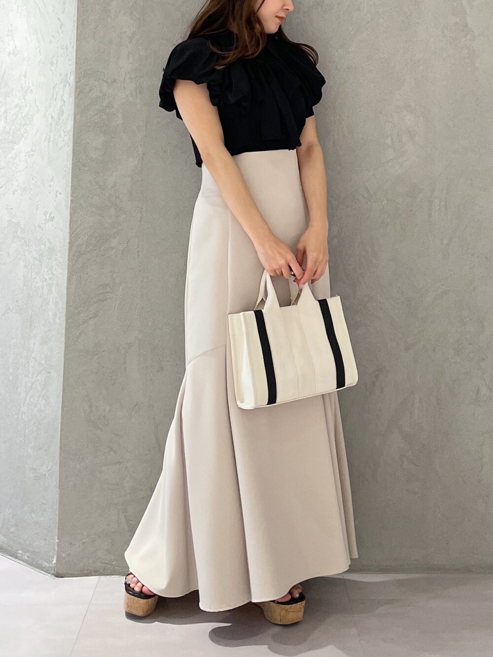 グレー系のハンドバッグ、ベージュ系のスカート、ブラック系のサンダルを着用したレディースの春コーディネートの2枚目の写真