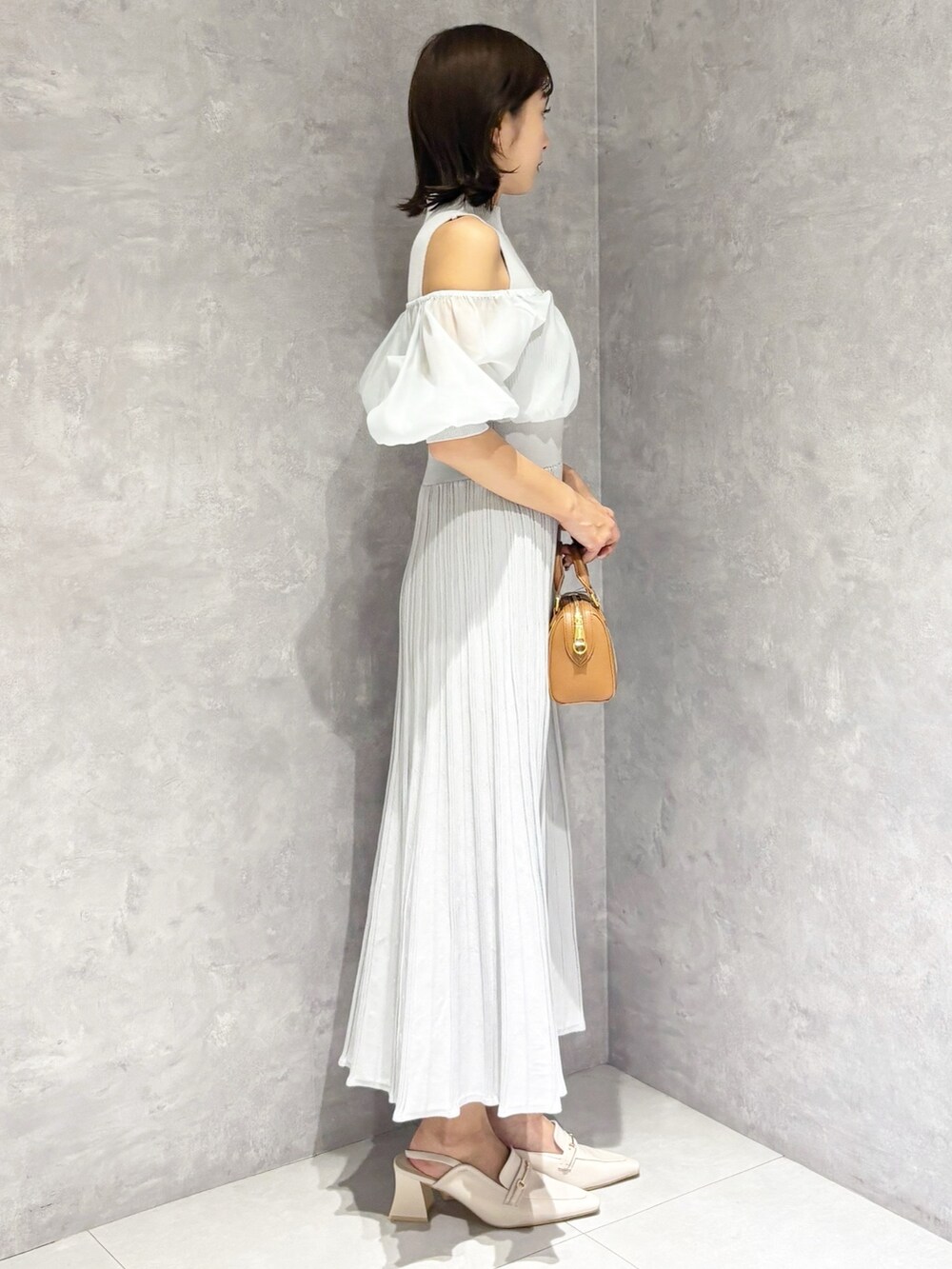 グレー系のワンピース、ホワイト系のパンプス、ブラウン系のハンドバッグを着用したレディースの春コーディネートの3枚目の写真