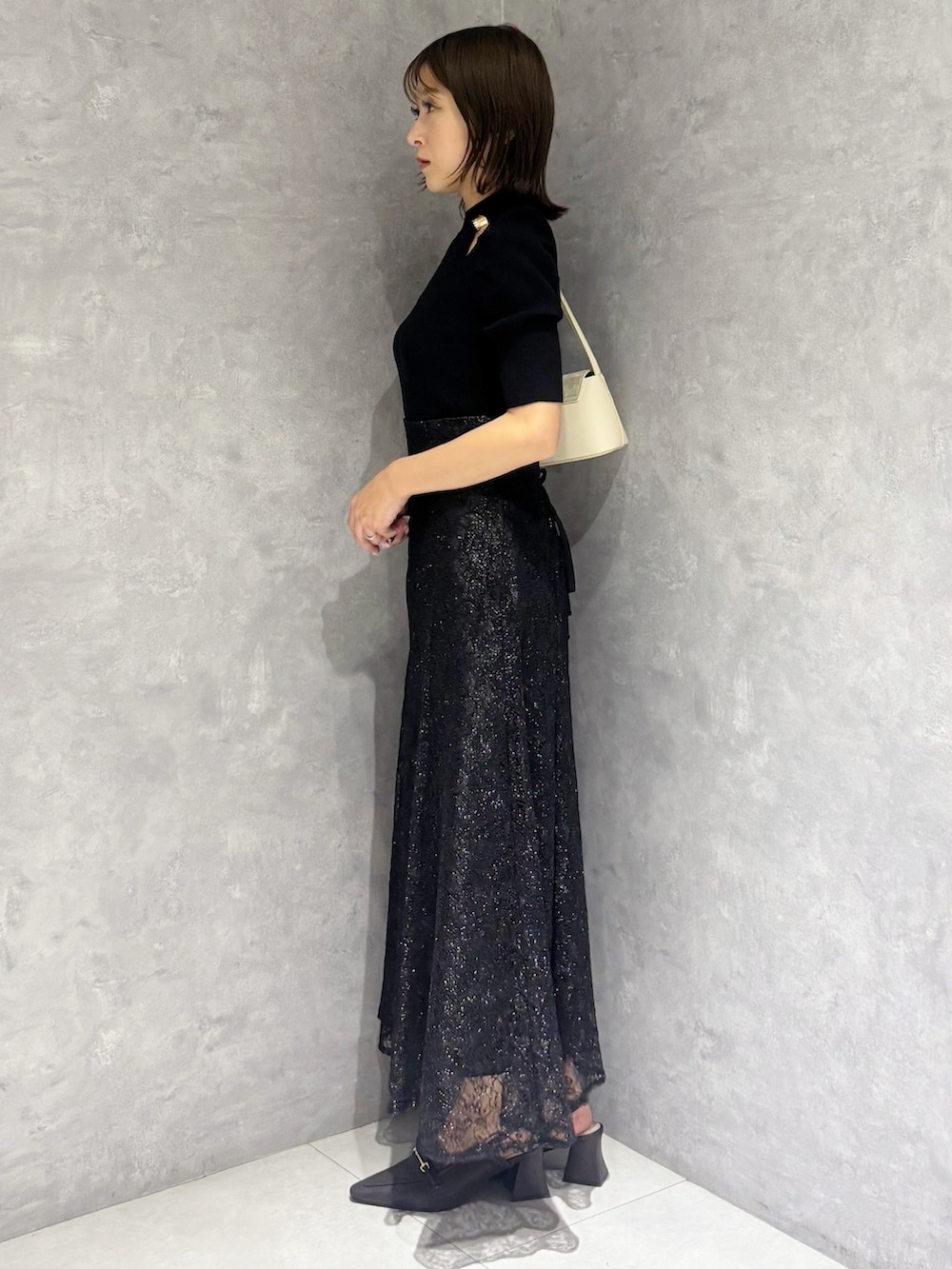 ブラック系のスカート、ブラック系のニット/セーター、ホワイト系のハンドバッグを着用したレディースの春コーディネートの2枚目の写真