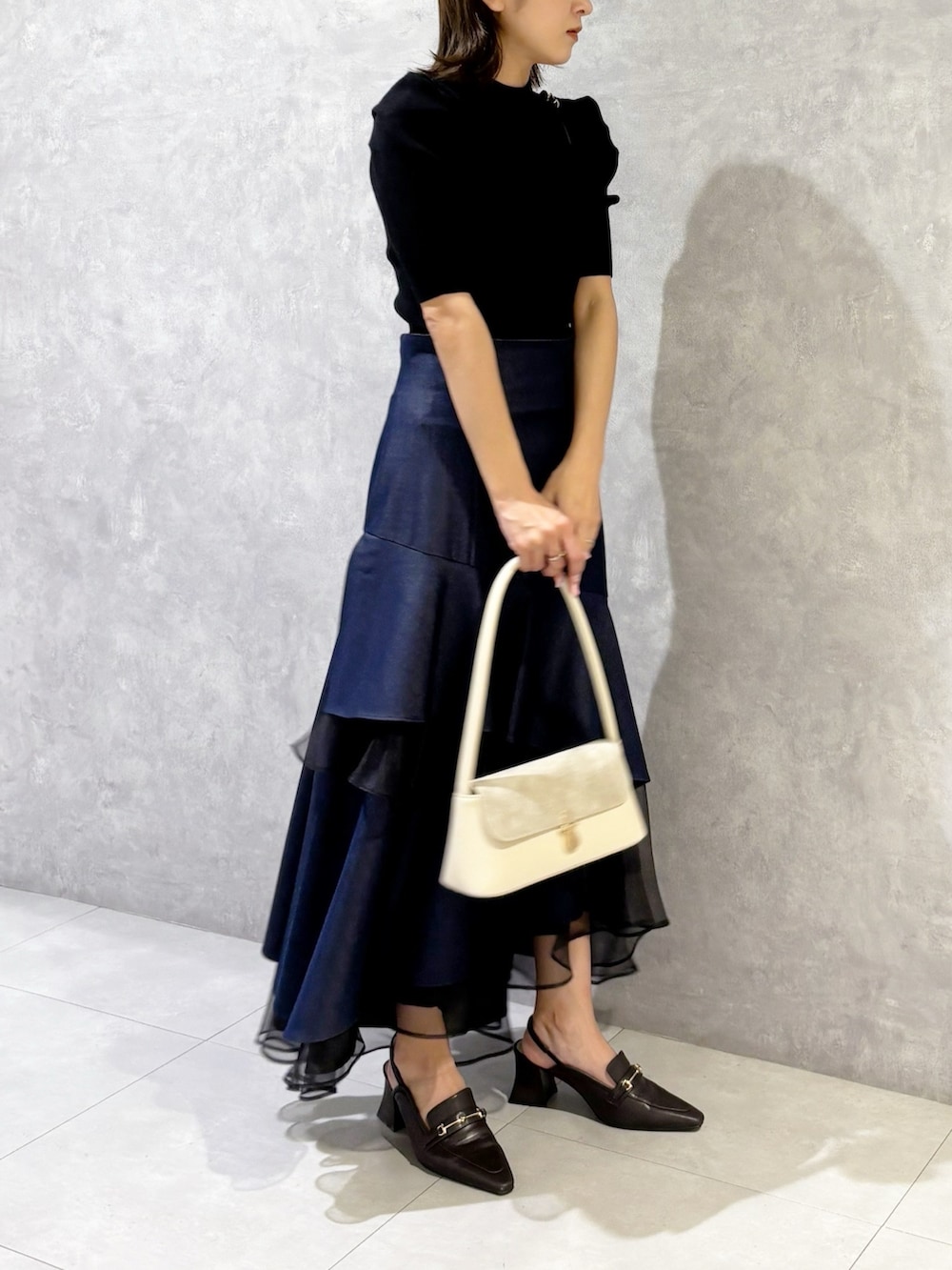 ブルー系のスカート、ブラック系のニット/セーター、ブラウン系のパンプスを着用したレディースの春コーディネートの4枚目の写真