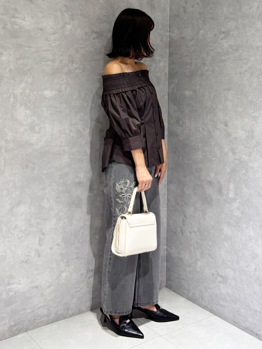 ホワイト系のハンドバッグ、ブラック系のパンプス、グレー系のデニムパンツを着用したレディースの夏コーディネートの2枚目の写真