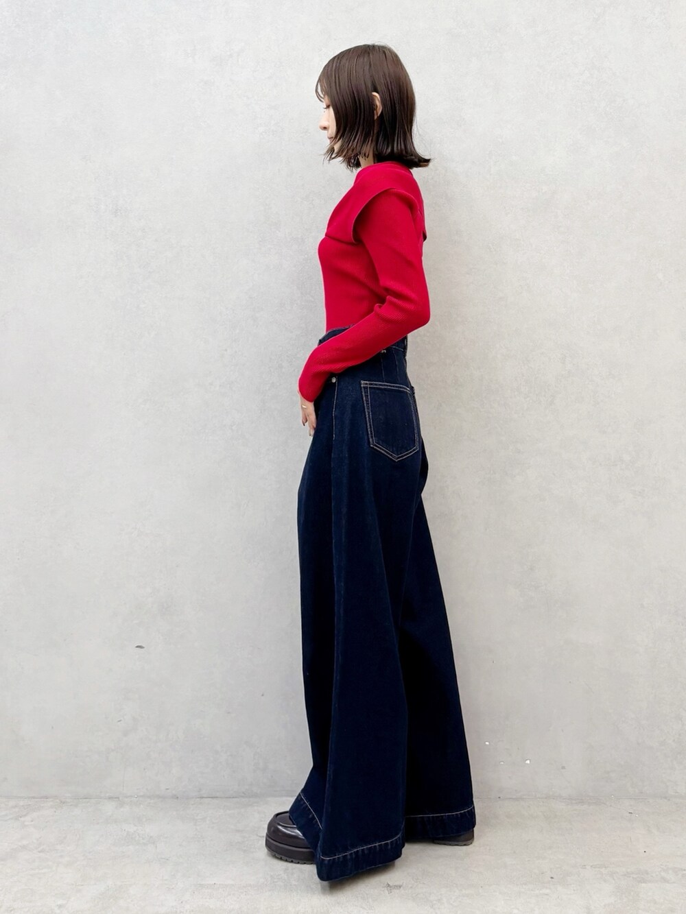 レッド系のニット/セーター、ブルー系のデニムパンツ、ブラウン系のブーツを着用したレディースの秋コーディネートの6枚目の写真