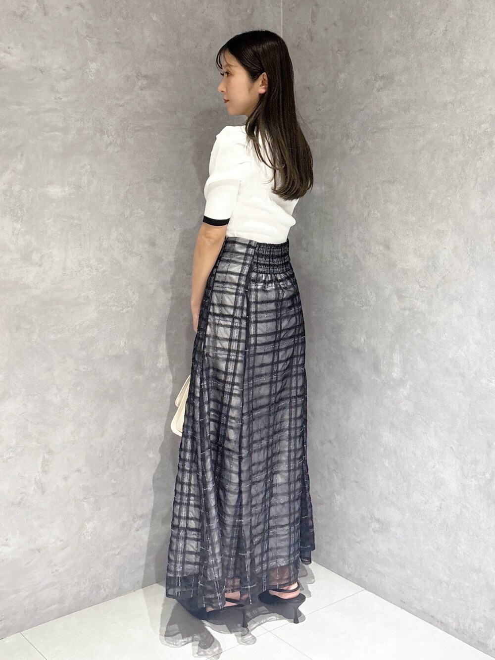 ブルー系のスカート、ブラック系のパンプス、ホワイト系のハンドバッグを着用したレディースの春コーディネートの3枚目の写真