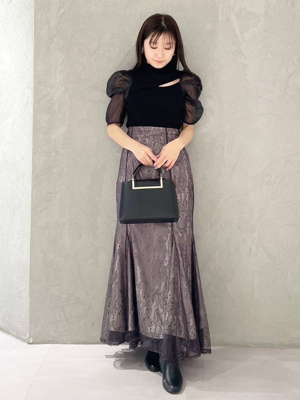 パープル系のスカート、ブラック系のハンドバッグ、ブラック系のニット/セーターを着用したレディースの春コーディネートの3枚目の写真