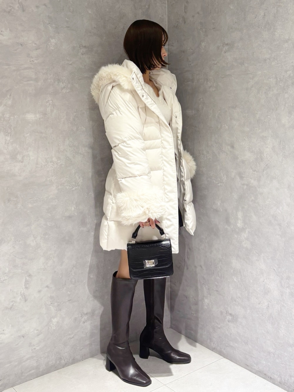 グレー系のスカート、ホワイト系のニット/セーター、ブラック系のハンドバッグを着用したレディースの冬コーディネートの2枚目の写真