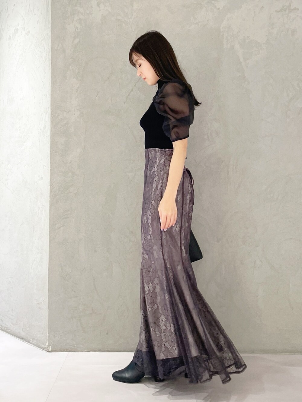 パープル系のスカート、ブラック系のハンドバッグ、ブラック系のニット/セーターを着用したレディースの春コーディネートの2枚目の写真