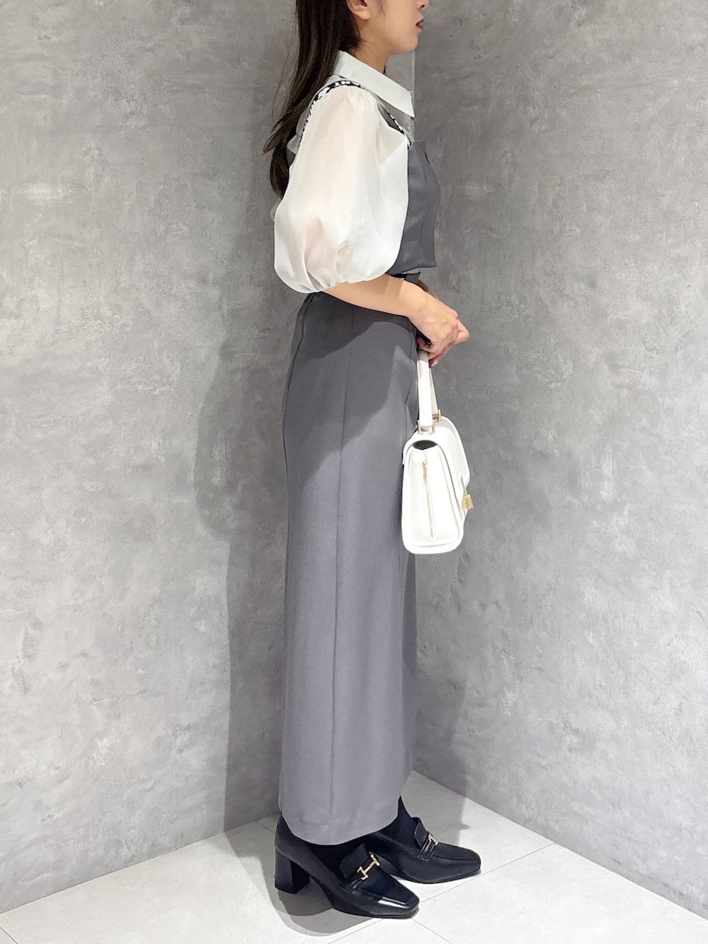 グレー系のスカート、ブラック系のブーツ、ホワイト系のハンドバッグを着用したレディースの春コーディネートの4枚目の写真